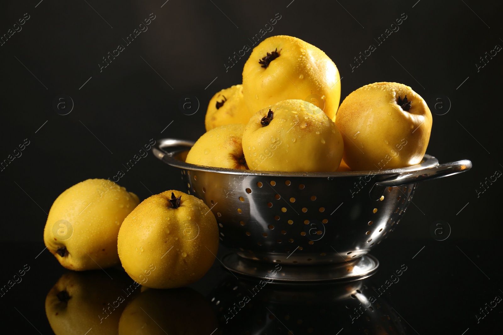 Photo of Tasty ripe quinces and metal colander on black mirror surface