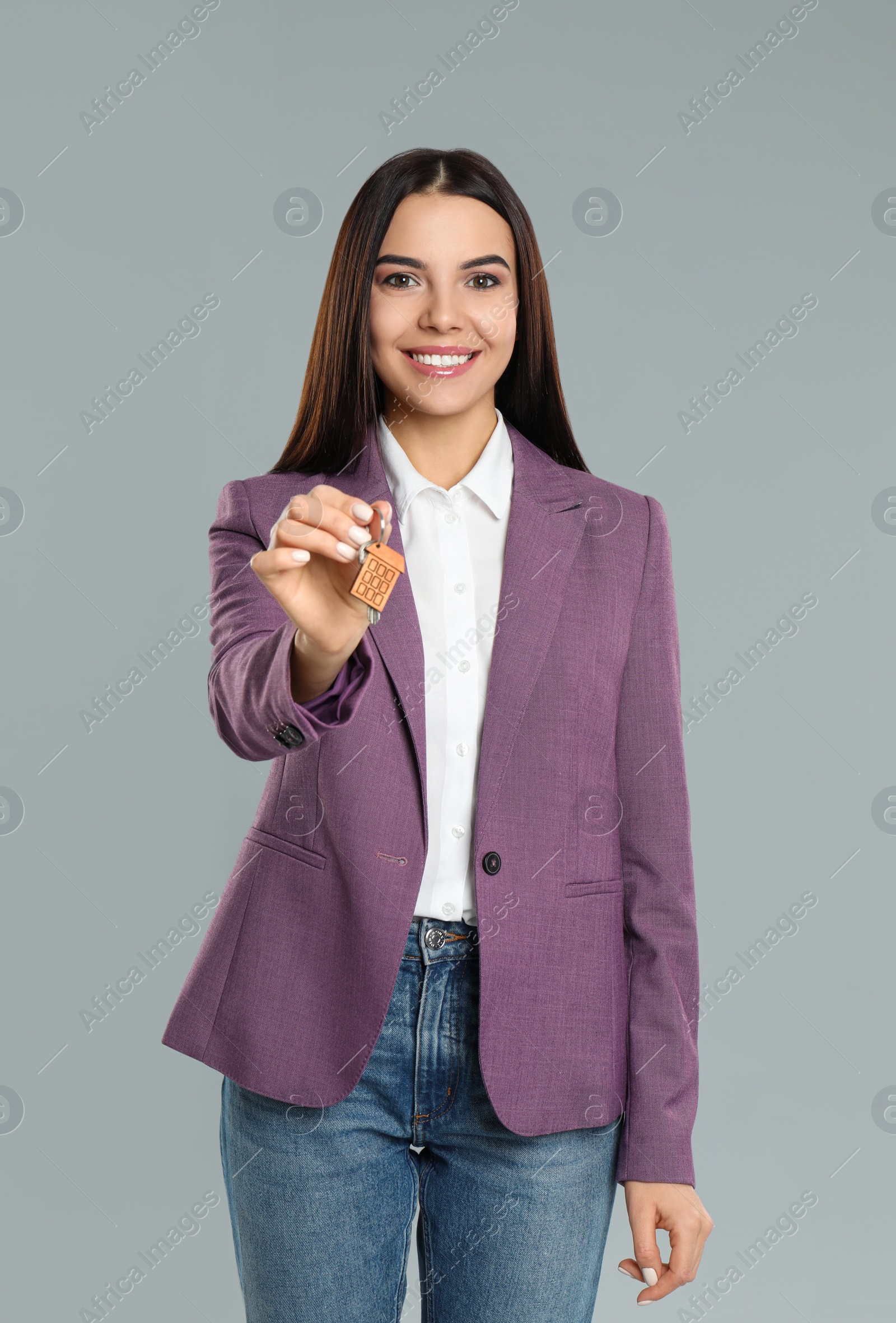Photo of Female real estate agent holding key on grey background