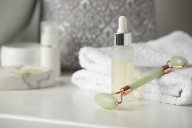 Photo of Natural face roller, towels and serum on counter in bathroom. Space for text