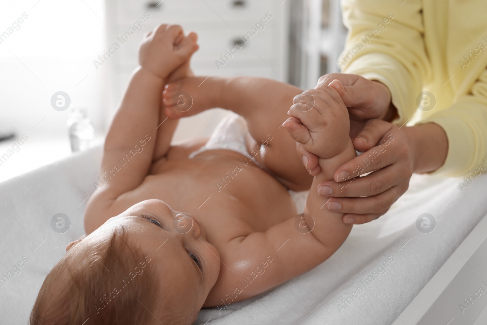 Photo of Mother massaging her baby with oil on changing table at home, closeup