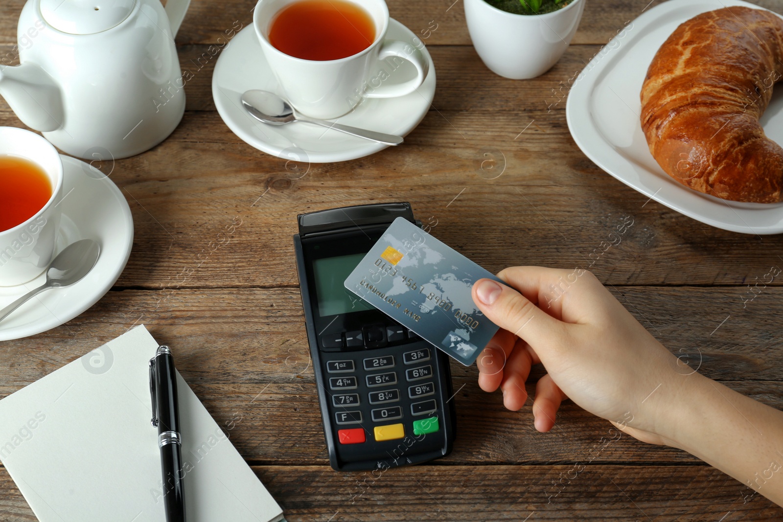 Photo of Woman with credit card using modern payment terminal at wooden table, closeup