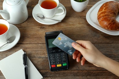 Woman with credit card using modern payment terminal at wooden table, closeup