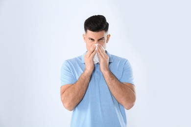 Man with tissue suffering from runny nose on white background