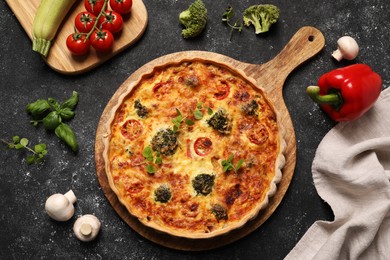 Delicious homemade quiche, oregano and different vegetables on black table, flat lay