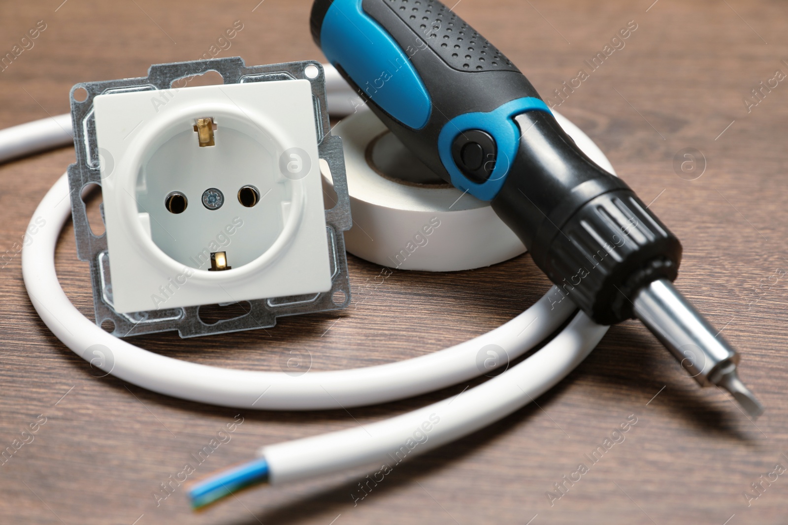 Photo of Screwdriver, cable, insulating tape and power socket on wooden table, closeup