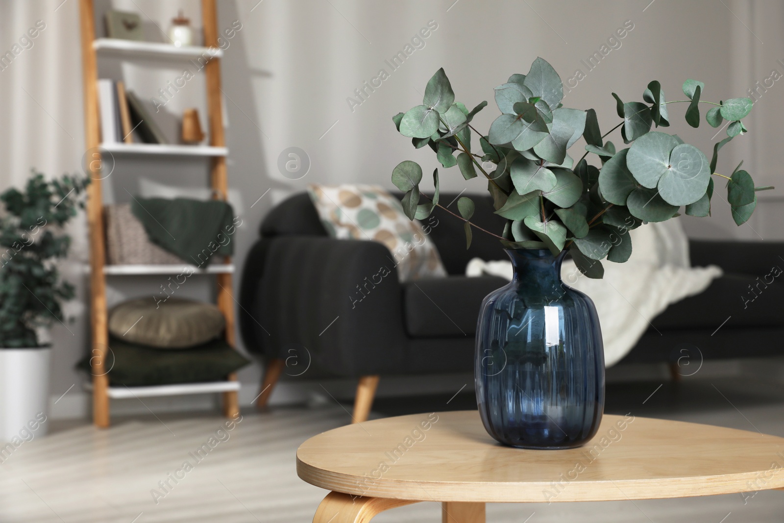 Photo of Blue glass vase with beautiful eucalyptus branches on wooden table in living room, space for text