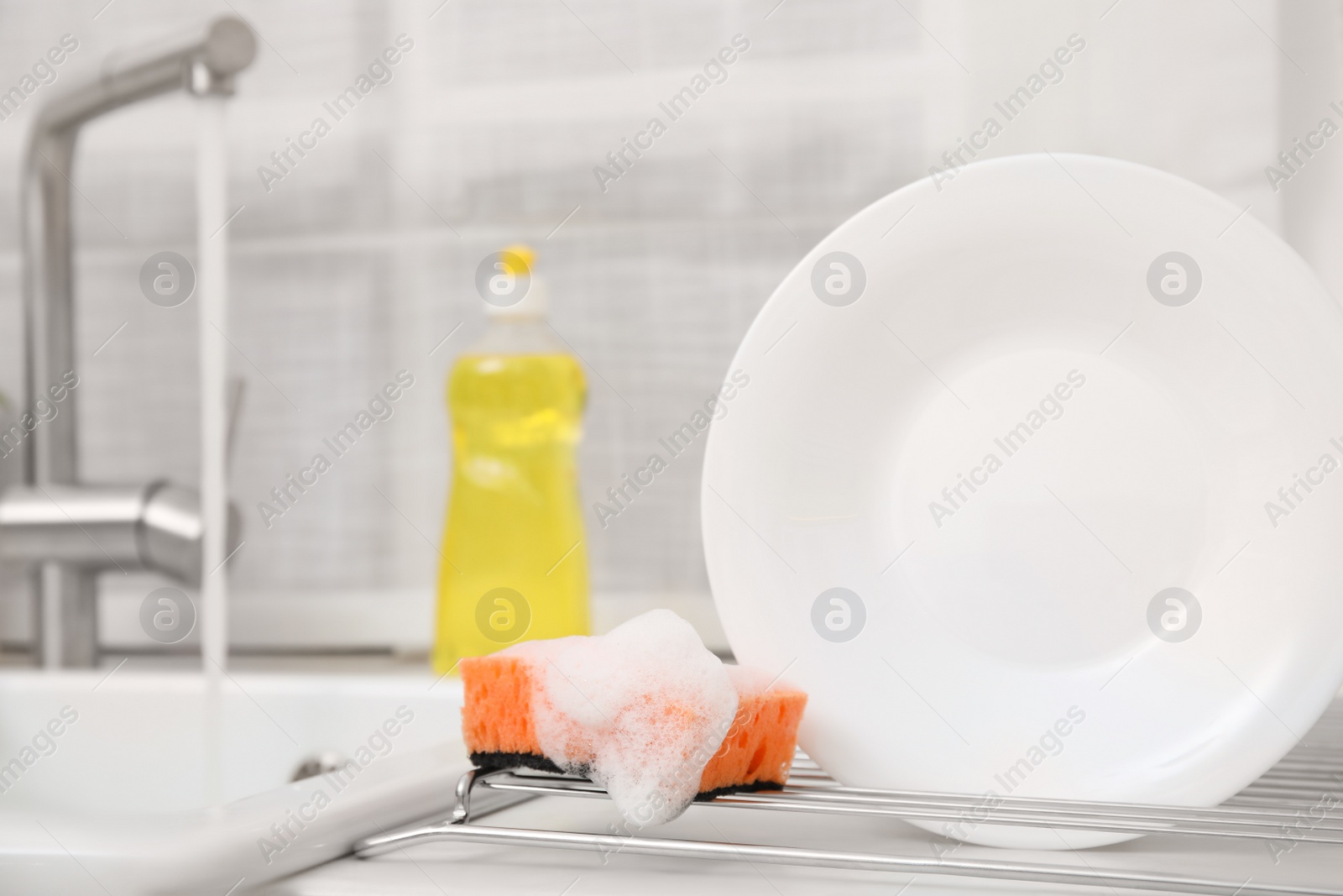 Photo of Drying rack with clean plate and soapy sponge in stylish kitchen