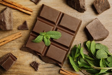 Tasty chocolate pieces, cinnamon sticks and mint on wooden table, flat lay