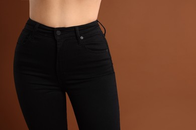 Woman wearing stylish black jeans on brown background, closeup. Space for text