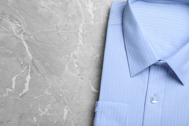 Photo of Stylish light blue shirt on grey marble table, top view with space for text. Dry-cleaning service