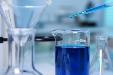 Photo of Laboratory analysis. Dripping blue liquid into beaker on table, closeup