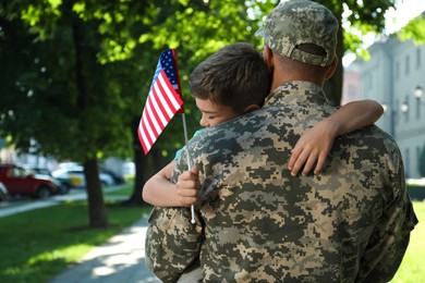 Soldier and his little son with flag of USA hugging outdoors