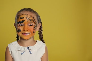 Photo of Cute little girl with face painting on orange background. Space for text