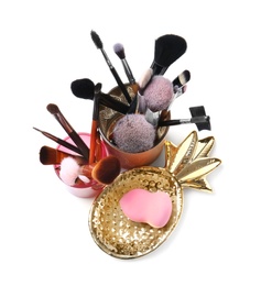 Holders with makeup brushes and sponge of professional artist on white background