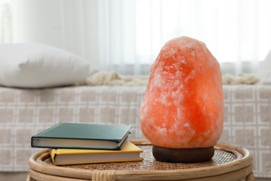 Photo of Beautiful Himalayan salt lamp and books on wicker table in bedroom, space for text