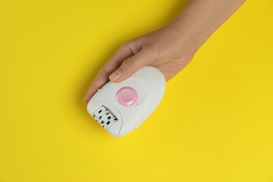 Woman holding modern epilator on yellow background, closeup