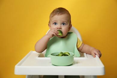 Photo of Cute little baby wearing bib while eating on yellow background