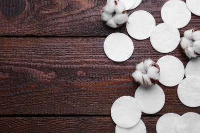 Photo of Flat lay composition with many clean cotton pads and flowers on wooden table. Space for text