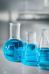 Photo of Different glassware with light blue liquid on table in laboratory