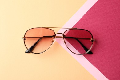 Stylish sunglasses on color background, top view