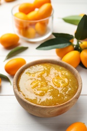 Delicious kumquat jam in bowl and fresh fruits on white wooden table