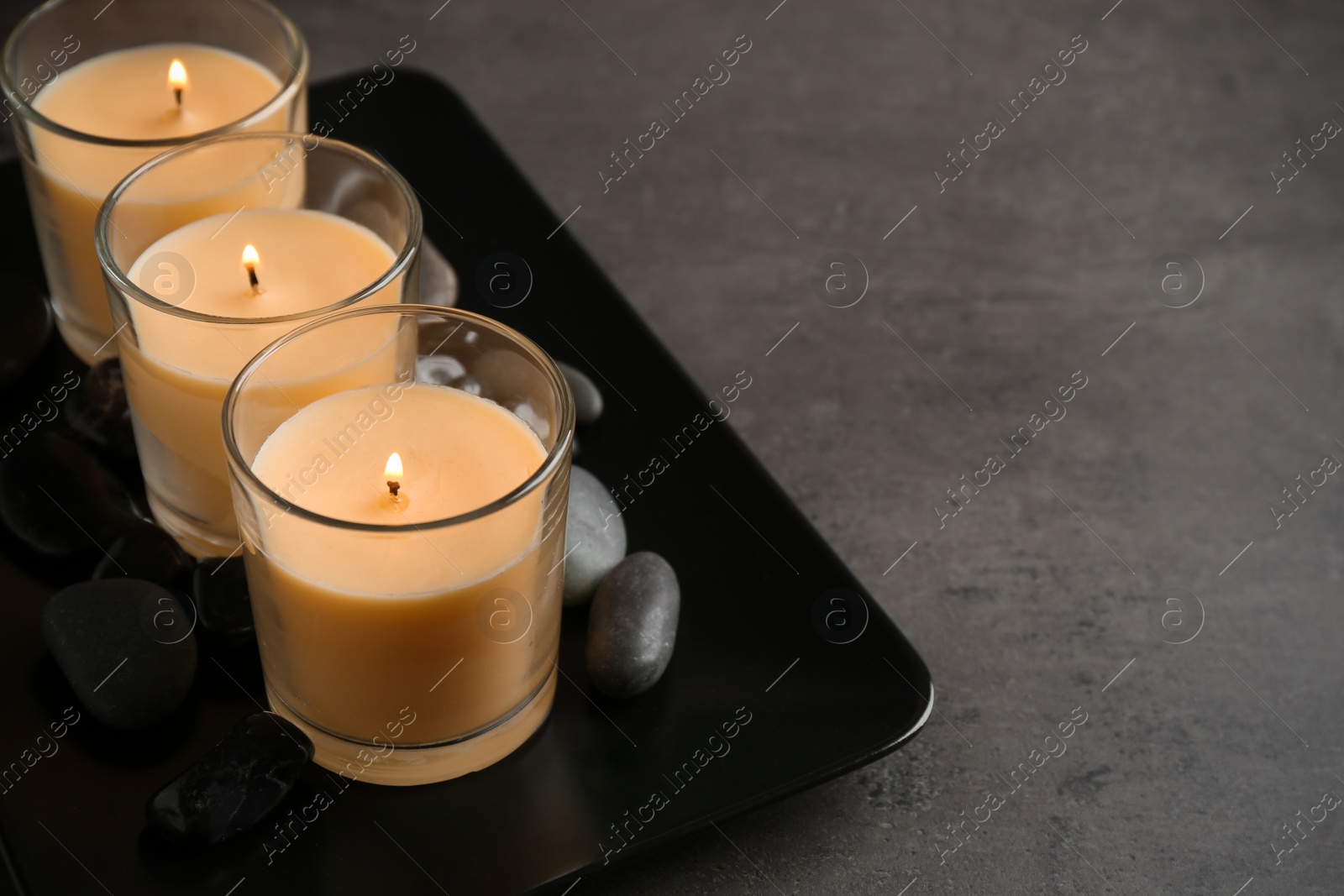 Photo of Dark plate with three burning candles and rocks on table, space for text