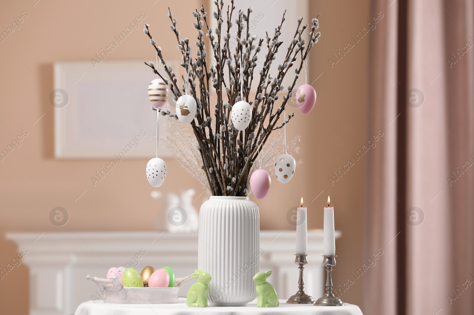 Photo of Pussy willow branches with festively decorated eggs, Easter bunnies and burning candles on table at home