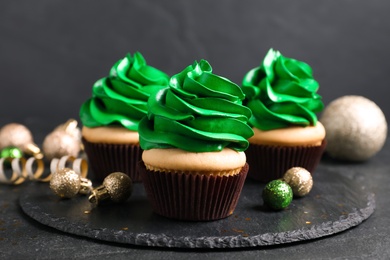 Delicious cupcakes with green cream and Christmas decor on black table