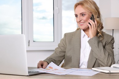 Photo of Lady boss talking on smartphone near laptop in office. Successful businesswoman