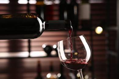 Pouring red wine from bottle into glass on blurred background, closeup