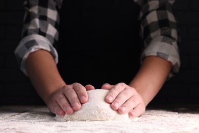 Photo of Man kneading dough at wooden table on dark background, closeup