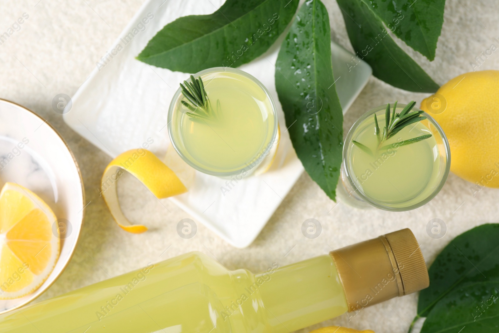 Photo of Tasty limoncello liqueur, lemons and green leaves on light textured table, flat lay