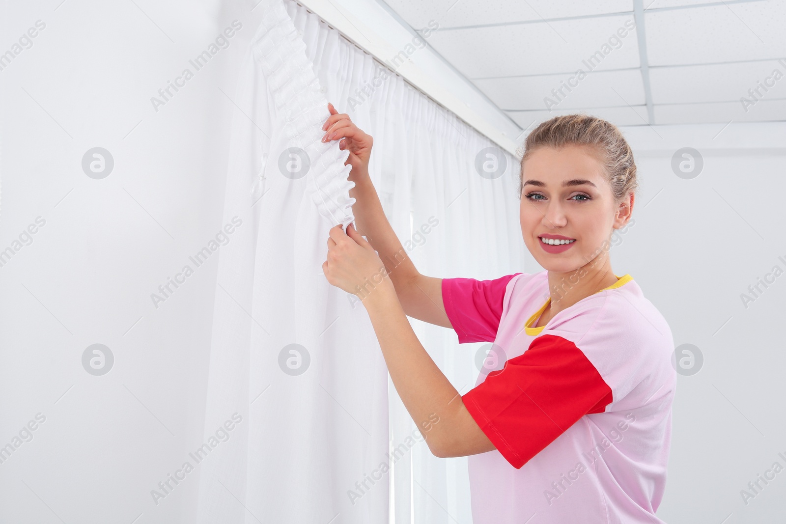 Photo of Woman hanging window curtain indoors. Interior decor element