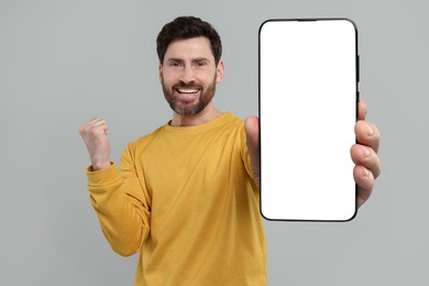 Image of Happy man holding smartphone with empty screen on grey background