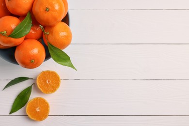 Bowl with fresh ripe juicy tangerines and green leaves on white wooden table, flat lay. Space for text