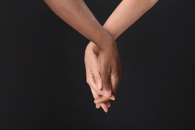 Woman and African American man holding hands on black background, closeup