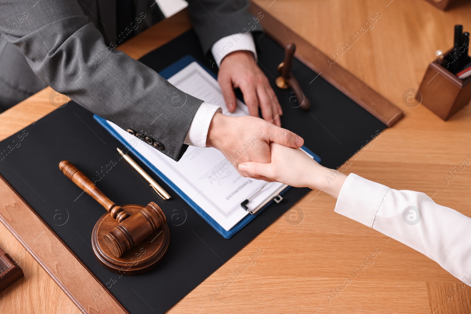 Photo of Notary shaking hands with client at wooden table, closeup