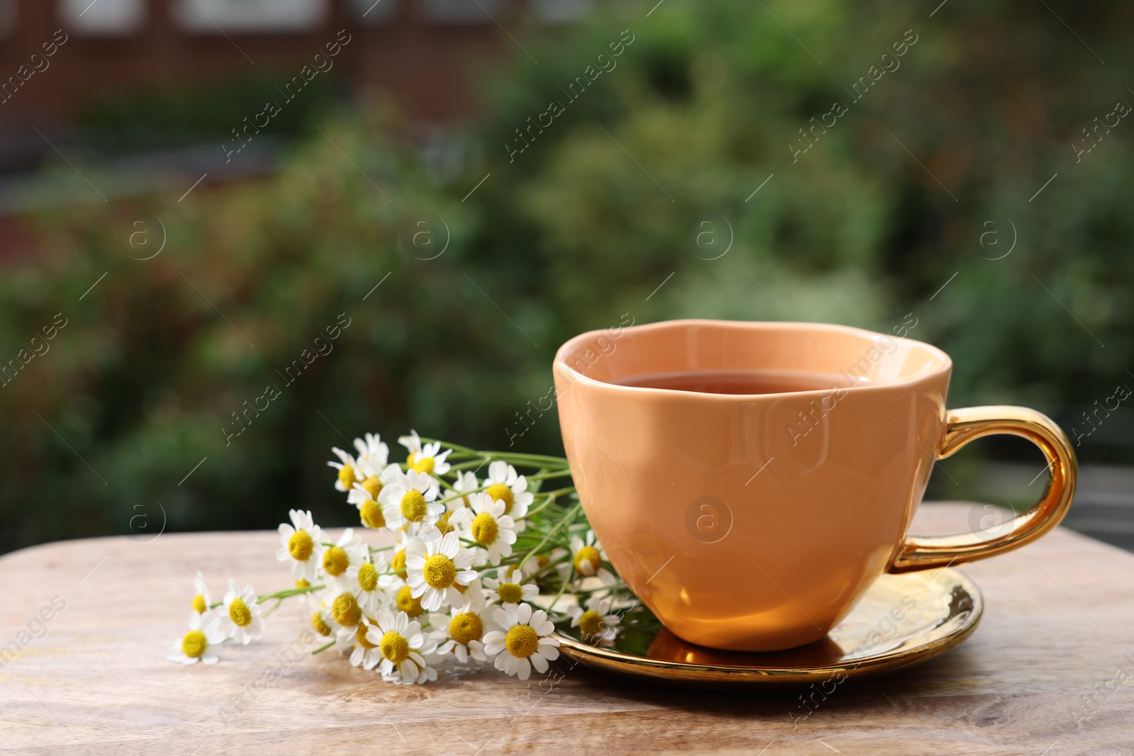 Photo of Cup of delicious chamomile tea and fresh flowers outdoors