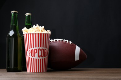 Photo of American football ball with popcorn and beer on wooden table. Space for text
