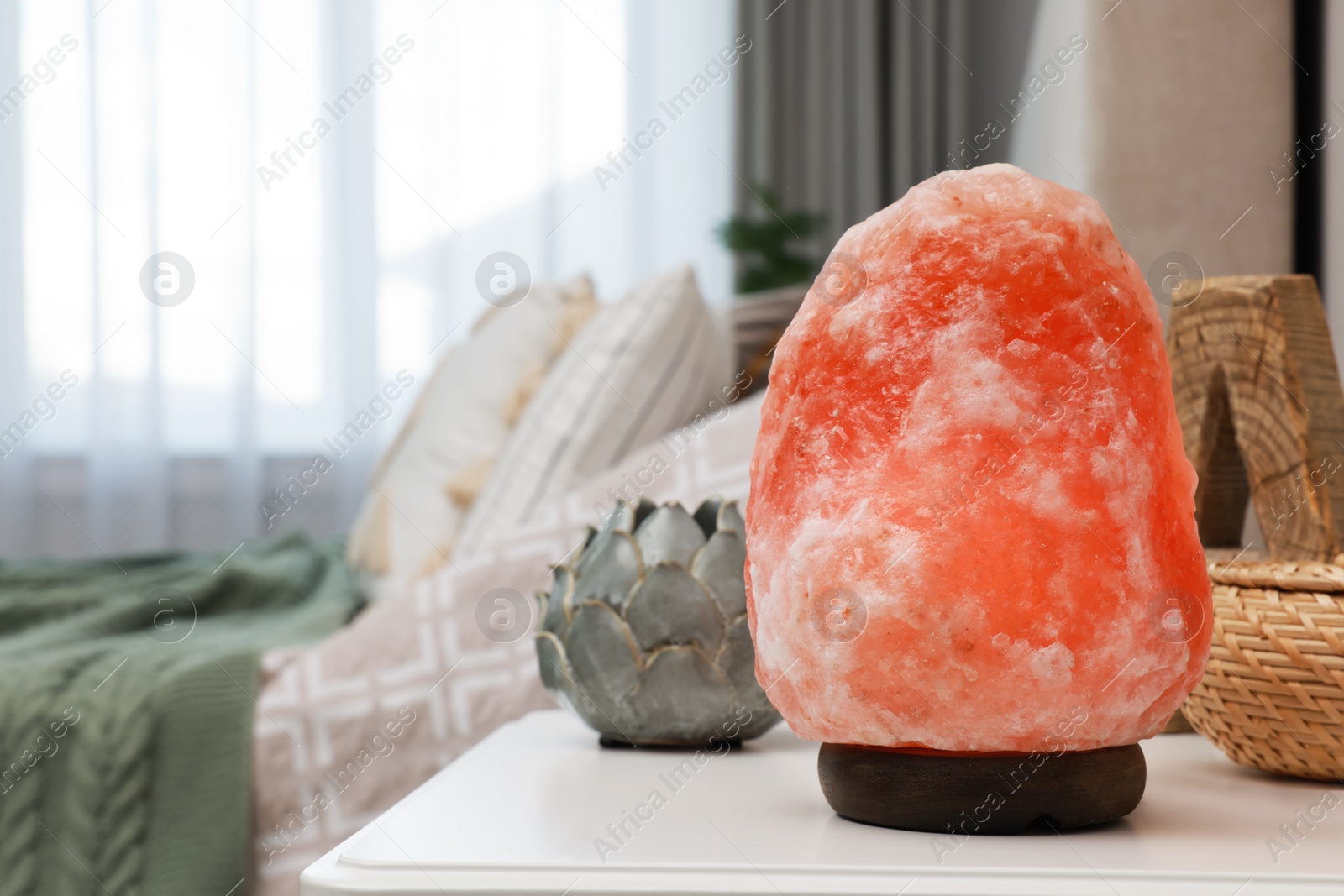 Photo of Beautiful Himalayan salt lamp, wicker box and lotus figure on white table in bedroom, space for text