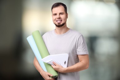 Man with wallpaper rolls and smoothing tool on blurred background