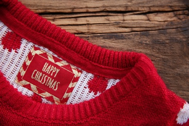 Photo of Christmas sweater with tag on wooden background, closeup