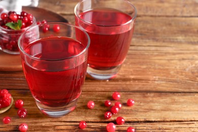 Photo of Tasty cranberry juice in glasses and fresh berries on wooden table. Space for text