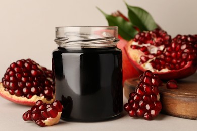 Glass jar of tasty pomegranate sauce and fresh ripe fruits on white background