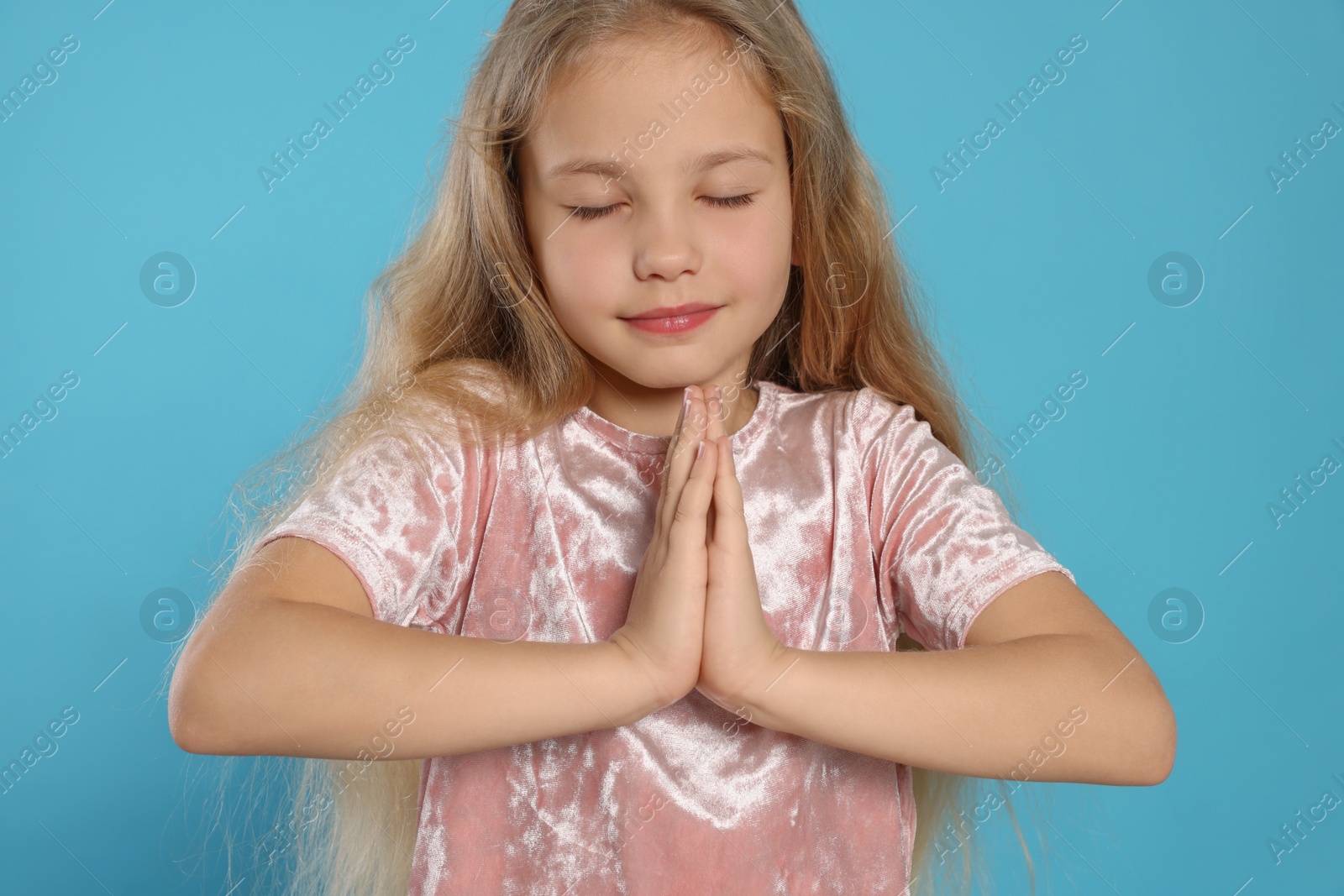 Photo of Beautiful girl with hands clasped together and closed eyes praying on light blue background