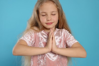 Beautiful girl with hands clasped together and closed eyes praying on light blue background