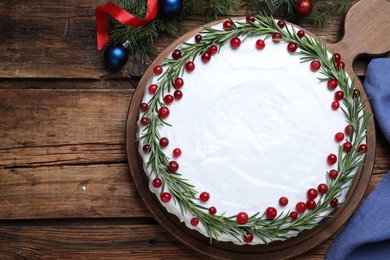Photo of Traditional Christmas cake decorated with rosemary and cranberries on wooden table, flat lay. Space for text