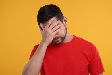Embarrassed man covering face on orange background