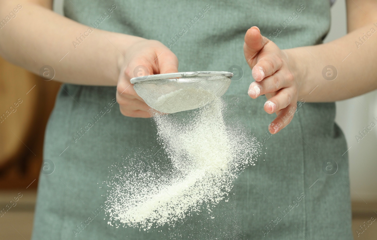 Photo of Woman sieving flour at table in kitchen, closeup