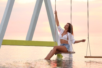 Photo of Young woman enjoying sunrise on swing over water